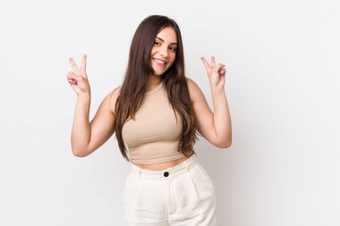 Genç ve güzel bir kadın gülümsüyor ve mutlu görünüyor, arkadaş canlısı ve memnun, işaret eden zafer ya da barış iki elle