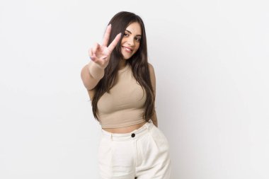 Genç ve güzel bir kadın gülümsüyor ve mutlu görünüyor, kaygısız ve pozitif, zafer ya da barış işareti yapıyor.