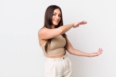 Genç, güzel bir kadın gülümsüyor, mutlu, pozitif ve tatmin olmuş hissediyor, fotokopi alanında nesne veya konsept tutuyor veya gösteriyor