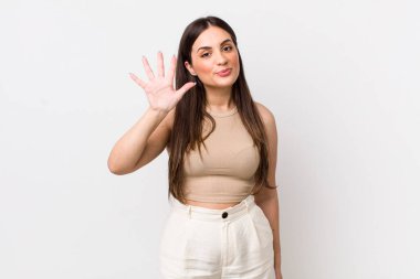 Genç ve güzel bir kadın gülümsüyor ve arkadaş canlısı görünüyor. 5 ya da 5 numarayı gösteriyor.
