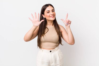 Genç ve güzel bir bayan gülümsüyor ve dost canlısı görünüyor, 7 ya da 7 numarayı gösteriyor, eli önde, geriye doğru sayıyor.