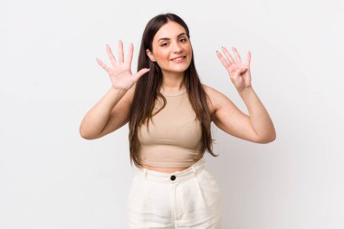 Genç, güzel bir kadın gülümsüyor ve dost canlısı görünüyor. 9 ya da 9 numarayı gösteriyor.