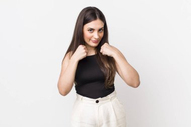 Genç ve güzel bir kadın kendinden emin, sinirli, güçlü ve agresif görünüyor. Yumrukları boks pozisyonunda dövüşmeye hazır.