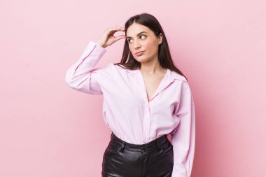 Genç, güzel bir kadın şaşkın ve kafası karışmış hissediyor, başını kaşıyor ve yan tarafa bakıyor.