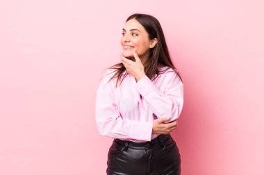 Genç, güzel bir kadın mutlu, kendinden emin bir ifadeyle gülümsüyor. Elleri çenesinde, merak ediyor ve yan tarafa bakıyor.