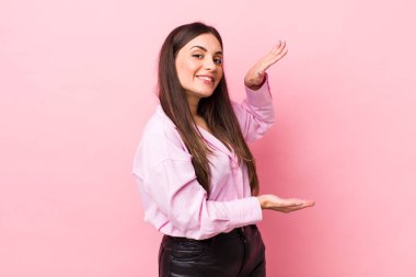 Genç, güzel bir kadın gülümsüyor, mutlu, pozitif ve tatmin olmuş hissediyor, fotokopi alanında nesne veya konsept tutuyor veya gösteriyor