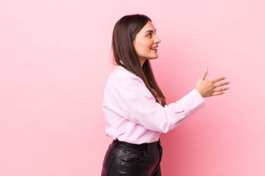 Genç, güzel bir kadın gülümsüyor, sizi selamlıyor ve başarılı bir anlaşma için el sıkışmayı teklif ediyor, işbirliği konsepti.