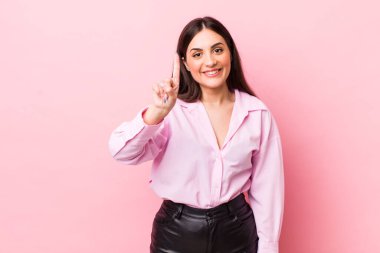 Genç ve güzel bir kadın gülümsüyor ve arkadaş canlısı görünüyor. Bir numarayı gösteriyor veya ilk eli önde, geriye doğru sayıyor.