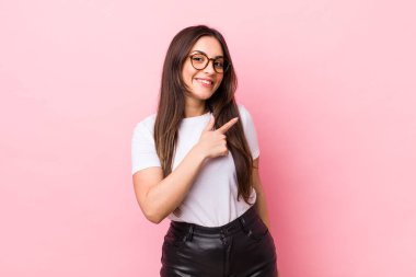 Genç, güzel bir kadın neşeli bir şekilde gülümsüyor, mutlu hissediyor ve kenarı ve yukarıyı işaret ediyor, kopyalama alanında nesneler gösteriyor.