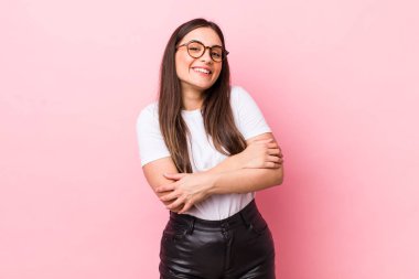 Genç ve güzel bir kadın kollarını kavuşturup mutlu bir şekilde gülüyor, rahat, pozitif ve tatmin edici bir pozla.