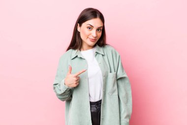 Genç ve güzel bir kadın gururlu, kendinden emin ve mutlu görünüyor, gülümsüyor ve kendini işaret ediyor ya da bir numaralı işareti yapıyor.