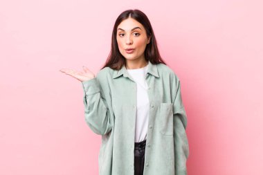 Genç ve güzel bir kadın şaşırmış ve şok olmuş görünüyor, çenesi düşmüş, bir objeyi elinde açık bir elle tutuyor.