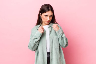 Genç ve güzel bir kadın kendinden emin, sinirli, güçlü ve agresif görünüyor. Yumrukları boks pozisyonunda dövüşmeye hazır.