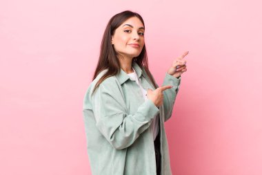 Genç ve güzel bir kadın neşeyle gülümsüyor ve yan taraftaki fotokopi alanını işaret ediyor, mutlu ve tatmin olmuş hissediyor.