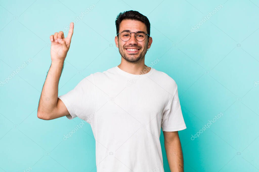 young handsome hicpanic man smiling cheerfully and happily, pointing upwards with one hand to copy space