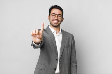 Genç, İspanyol bir adam gülümsüyor ve arkadaş canlısı görünüyor. Bir numarayı gösteriyor. iş kavramı