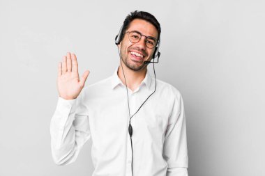 Genç, Latin asıllı, mutlu bir şekilde gülümseyen, el sallayan, sizi selamlayan genç bir adam. tele pazarlamacı kavramı