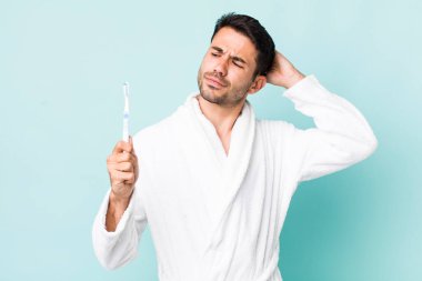 young adult hispanic man feeling puzzled and confused, scratching head. toothbrush concept