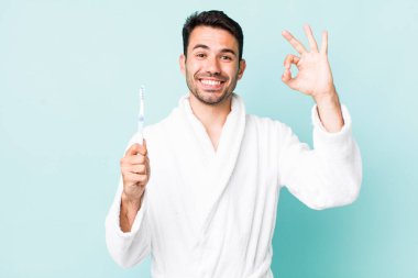 young adult hispanic man feeling happy, showing approval with okay gesture. toothbrush concept