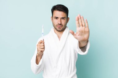 young adult hispanic man looking serious showing open palm making stop gesture. toothbrush concept
