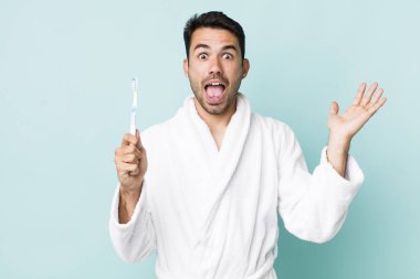 young adult hispanic man feeling happy and astonished at something unbelievable. toothbrush concept