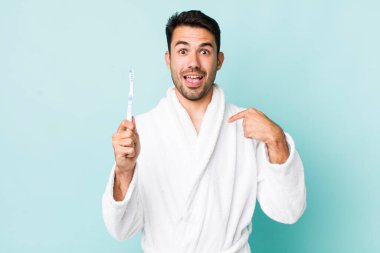 young adult hispanic man feeling happy and pointing to self with an excited. toothbrush concept