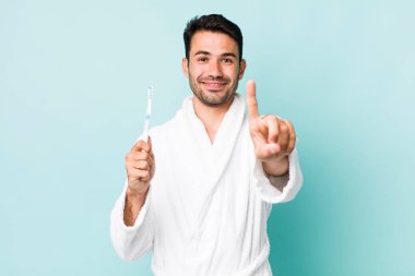 young adult hispanic man smiling proudly and confidently making number one. toothbrush concept
