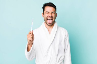 young adult hispanic man with cheerful and rebellious attitude, joking and sticking tongue out. toothbrush concept