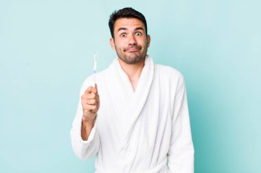 young adult hispanic man shrugging, feeling confused and uncertain. toothbrush concept