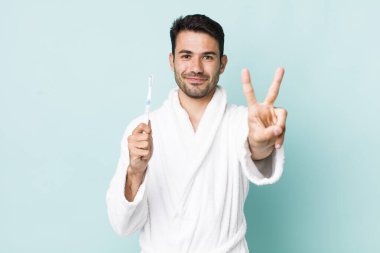 young adult hispanic man smiling and looking friendly, showing number two. toothbrush concept