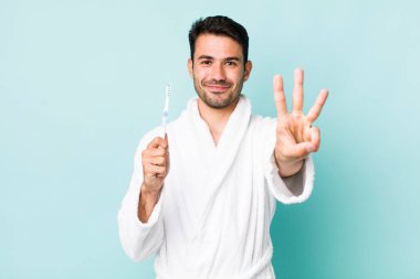young adult hispanic man smiling and looking friendly, showing number three. toothbrush concept