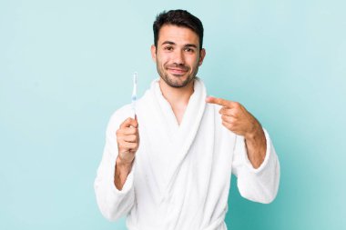 young adult hispanic man smiling cheerfully, feeling happy and pointing to the side. toothbrush concept