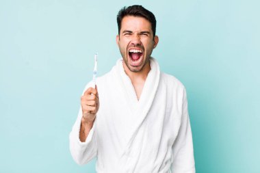 young adult hispanic man shouting aggressively, looking very angry. toothbrush concept