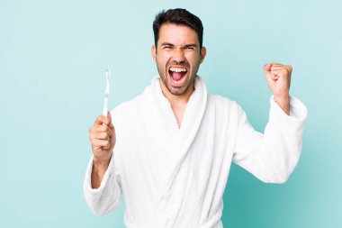 young adult hispanic man shouting aggressively with an angry expression. toothbrush concept