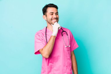 young adult hispanic man smiling with a happy, confident expression with hand on chin. veterinarian concept