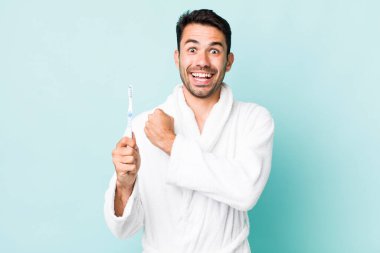 young adult hispanic man feeling happy and facing a challenge or celebrating. toothbrush concept