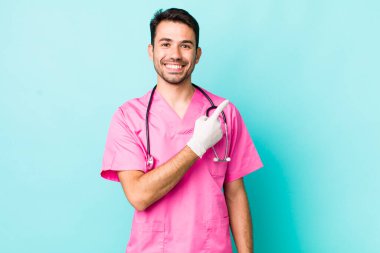 young adult hispanic man smiling cheerfully, feeling happy and pointing to the side. veterinarian concept