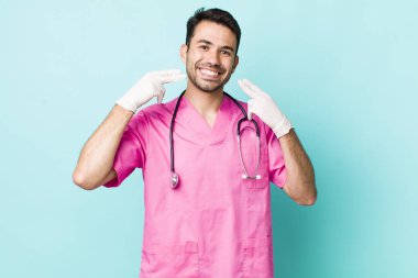 young adult hispanic man smiling confidently pointing to own broad smile. veterinarian concept