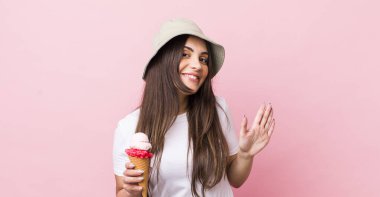 young pretty woman smiling happily, waving hand, welcoming and greeting you. summer and ice cream concept