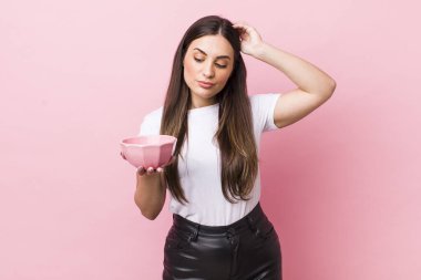 young pretty woman feeling puzzled and confused, scratching head. empty bowl concept