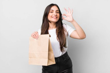 young pretty woman feeling happy, showing approval with okay gesture. take away food concept