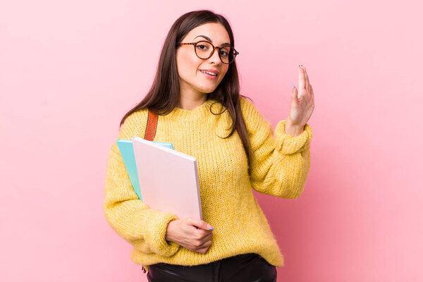 young pretty woman smiling happily, waving hand, welcoming and greeting you. university student concept