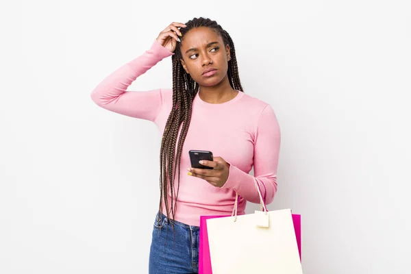 Young Adult Black Woman Smiling Happily Daydreaming Doubting Shopping Bags — Stockfoto