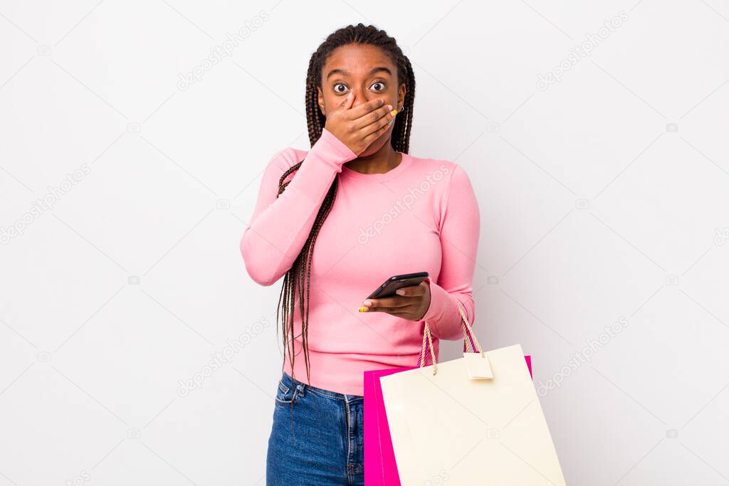 young adult black woman covering mouth with hands with a shocked. shopping bags concept