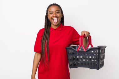 young adult black woman with cheerful and rebellious attitude, joking and sticking tongue out. empty shopping basket concept
