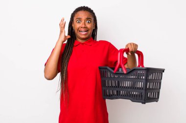 young adult black woman screaming with hands up in the air. empty shopping basket concept