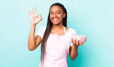 young adult black woman feeling happy, showing approval with okay gesture. empty bowl concept