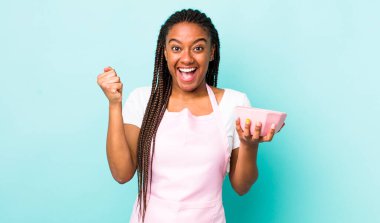 young adult black woman feeling shocked,laughing and celebrating success. empty bowl concept