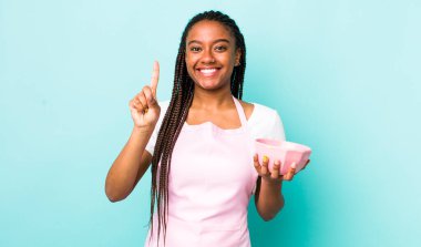 young adult black woman smiling and looking friendly, showing number one. empty bowl concept