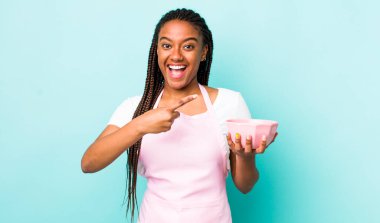 young adult black woman looking excited and surprised pointing to the side. empty bowl concept